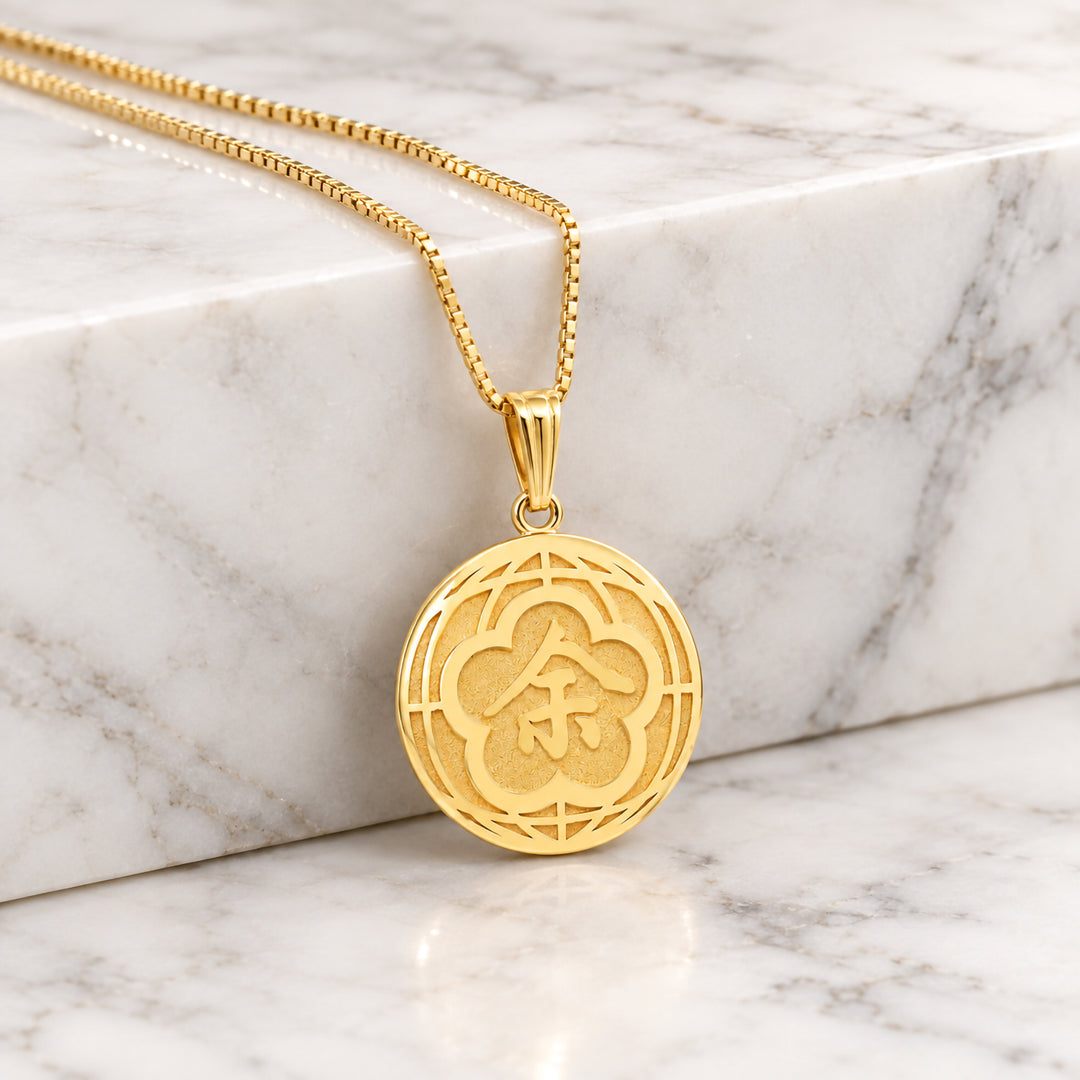 Finished 14 karat yellow gold round name pendant with polished raised design over a textured background, hanging on a box chain