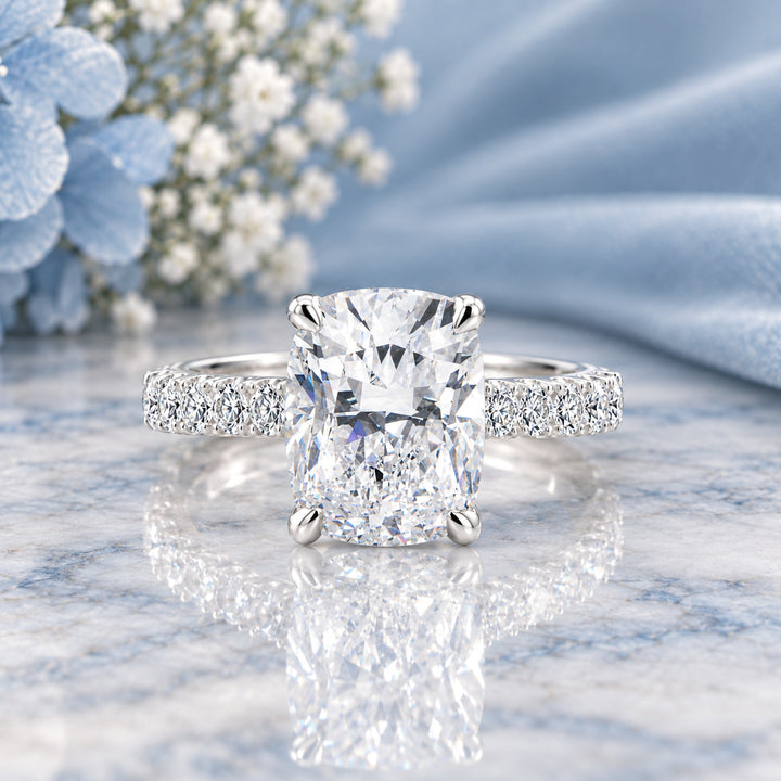 14 karat white gold 3ct elongated cushion lab grown diamond hidden halo engagement ring with diamond accent band shown from the front on a styled display at AJ's Jewelry in Ridgewood, Queens NY
