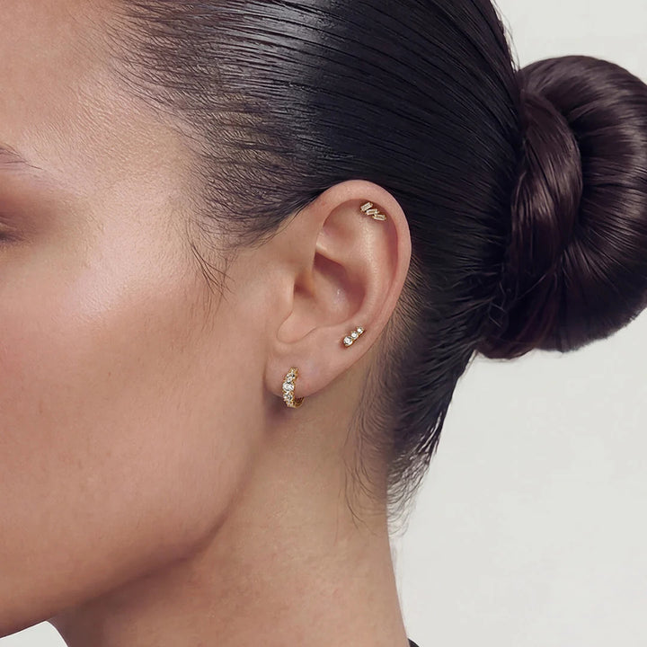 Close-up of the 14K yellow gold baguette lab grown diamond three-stone stud earrings worn on the ear | AJ's Jewelry