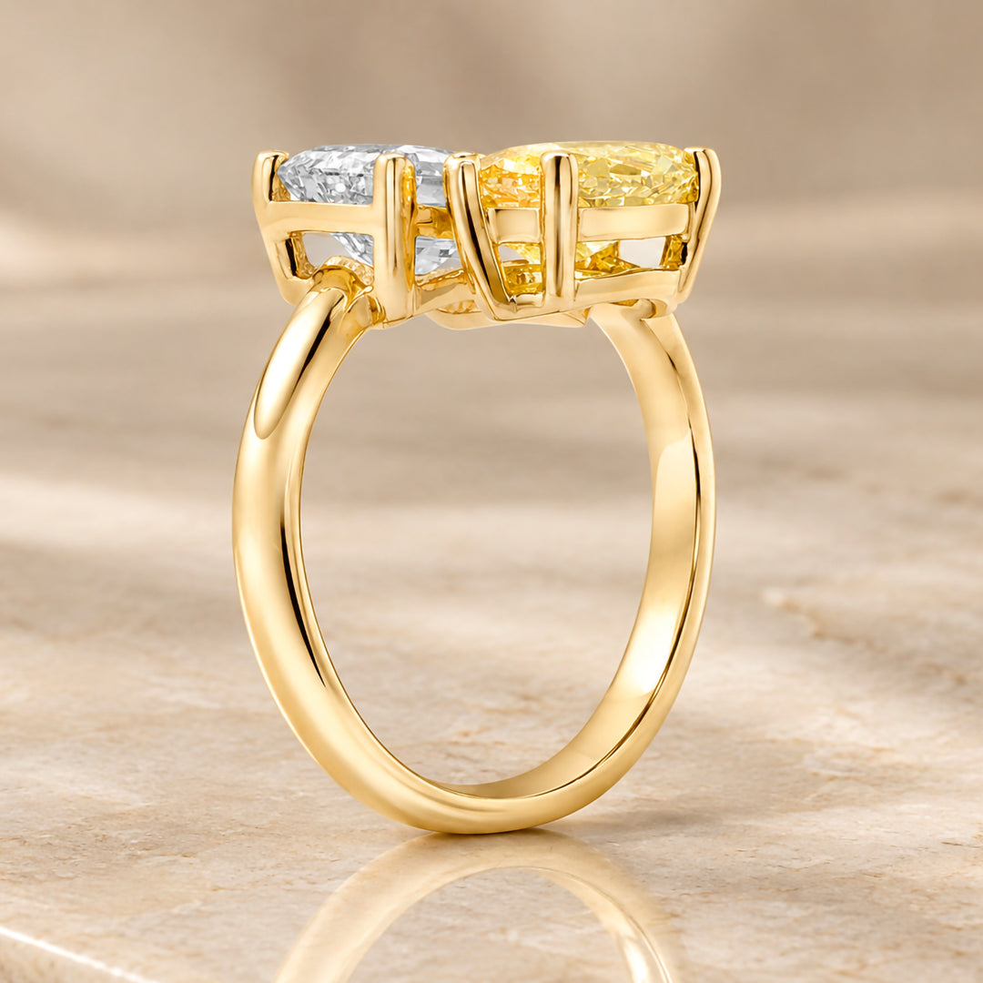 14 karat yellow gold toi et moi engagement ring with a 3ct emerald shape lab grown diamond and a fancy vivid yellow marquise lab grown diamond shown from the side on a styled display at AJ's Jewelry in Ridgewood, Queens NY