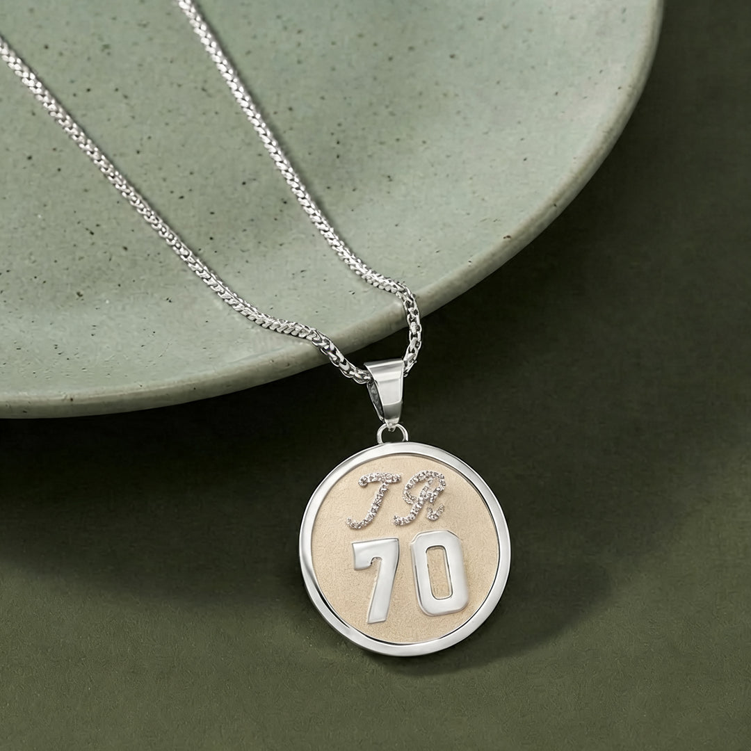Styled photograph of the custom two-tone diamond initial and number 70 pendant resting beside a ceramic dish at AJ's Jewelry