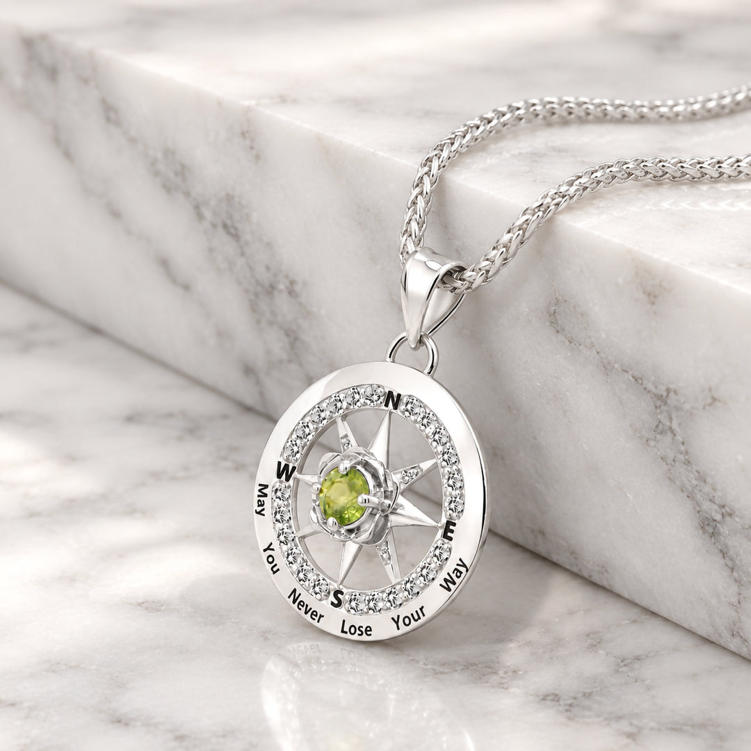 Angled view of the white gold compass rose pendant showing the phrase May You Never Lose Your Way in black enamel lettering