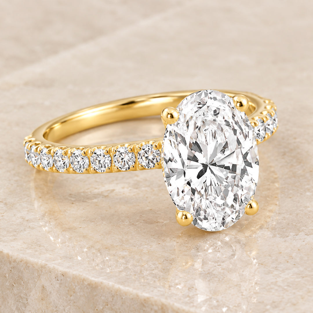 18 karat yellow gold 2ct oval lab grown diamond hidden halo engagement ring with diamond accent band shown at an angle on a styled display at AJ's Jewelry in Ridgewood, Queens NY