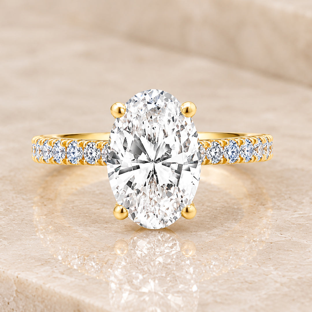 18 karat yellow gold 2ct oval lab grown diamond hidden halo engagement ring with diamond accent band shown from the front on a styled display at AJ's Jewelry in Ridgewood, Queens NY