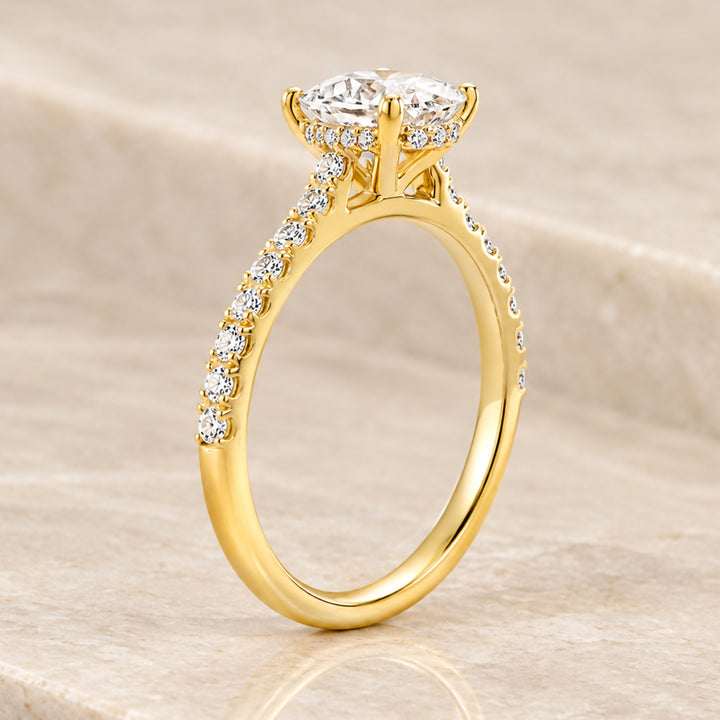 18 karat yellow gold 2ct oval lab grown diamond hidden halo engagement ring with diamond accent band shown from the side on a styled display at AJ's Jewelry in Ridgewood, Queens NY