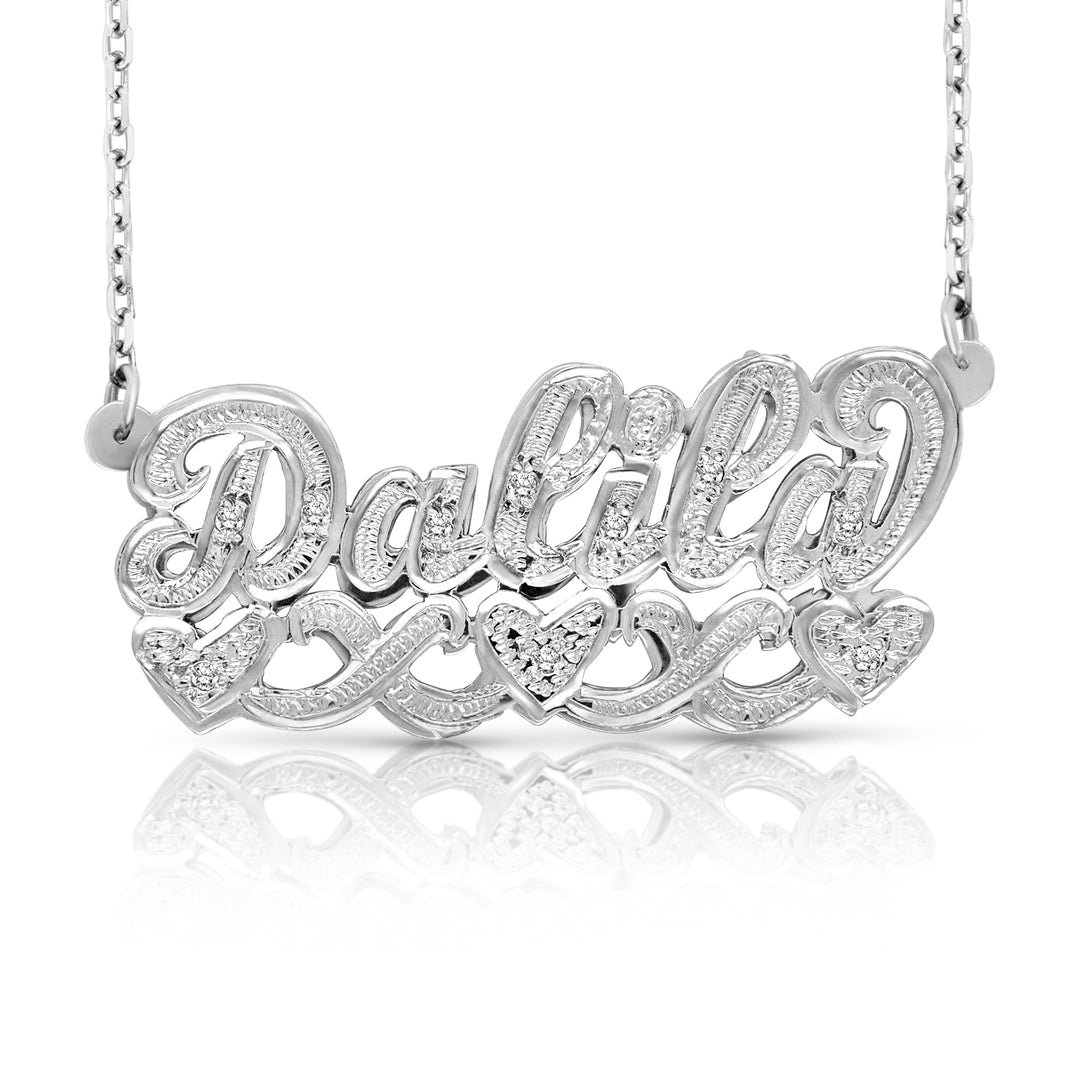 A silver personalized name necklace spelling 'Dakota' in cursive, adorned with small clear stones, hanging from a matching silver chain against a white background with a soft reflection below.