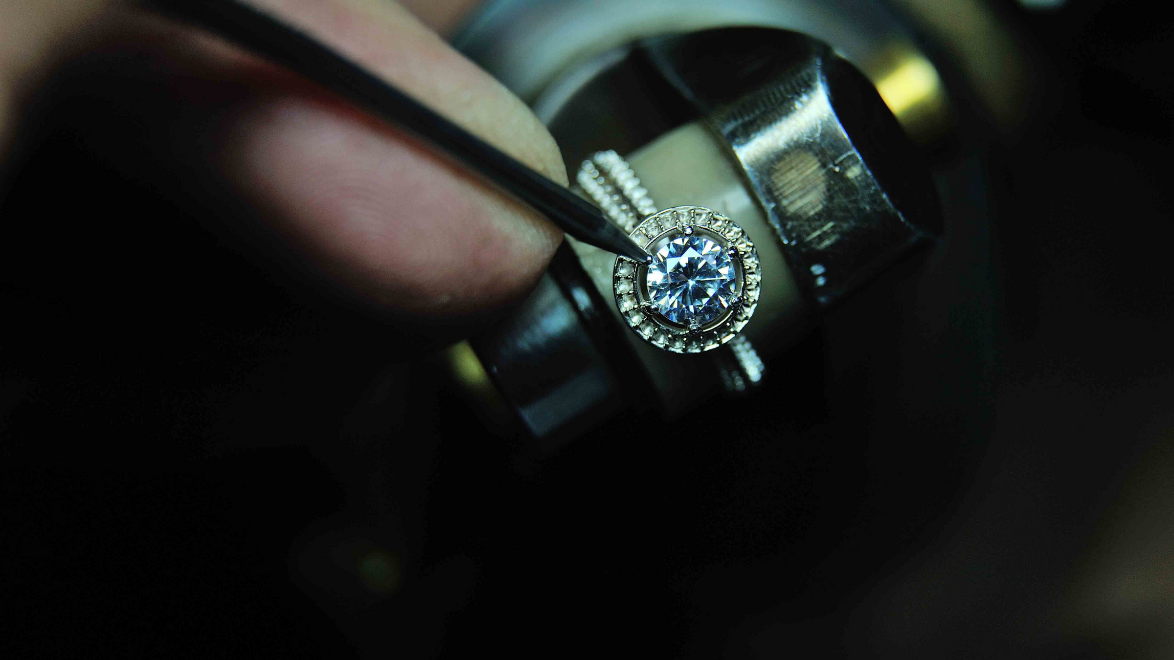 A jeweler using a tool to retip a prong on a diamond ring