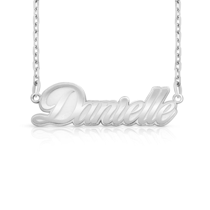 A silver nameplate necklace spelling 'Danielle' in cursive script, suspended from a delicate silver chain against a white background with a soft reflection below.  This photo can change appearance depending on the name input using the custom name builder