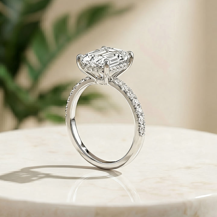 Custom 14KT white gold hidden halo emerald-shape lab-grown diamond engagement ring shown from the side on a styled display at AJ's Jewelry in Ridgewood, Queens NY