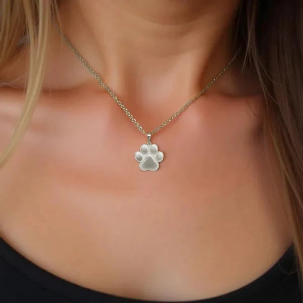 A white gold paw print pendant necklace worn on a model's neck, shown in a close-up shot.