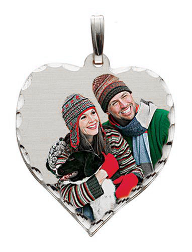 A heart-shaped silver pendant with a custom photo insert showing a smiling couple in winter clothing, complete with a silver bail at the top, set against a plain white background.